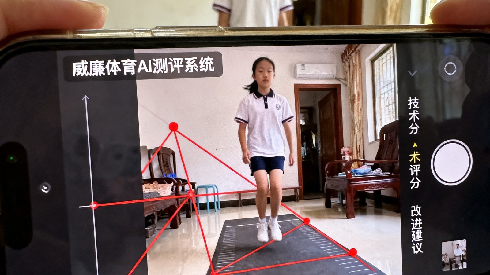 一名初三女生在家中用手机拍摄自己的立定跳远动作，手机屏幕上显示着威廉体育AI测评系统的分析界面，红色线条标注出她的起跳角度和身体重心轨迹，右侧显示着技术评分和改进建议。